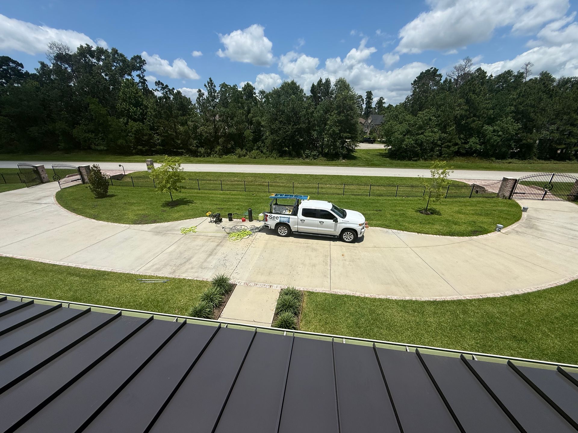 White utility truck parked on a circular gravel drive beside a grassy field and trees under a blue sky