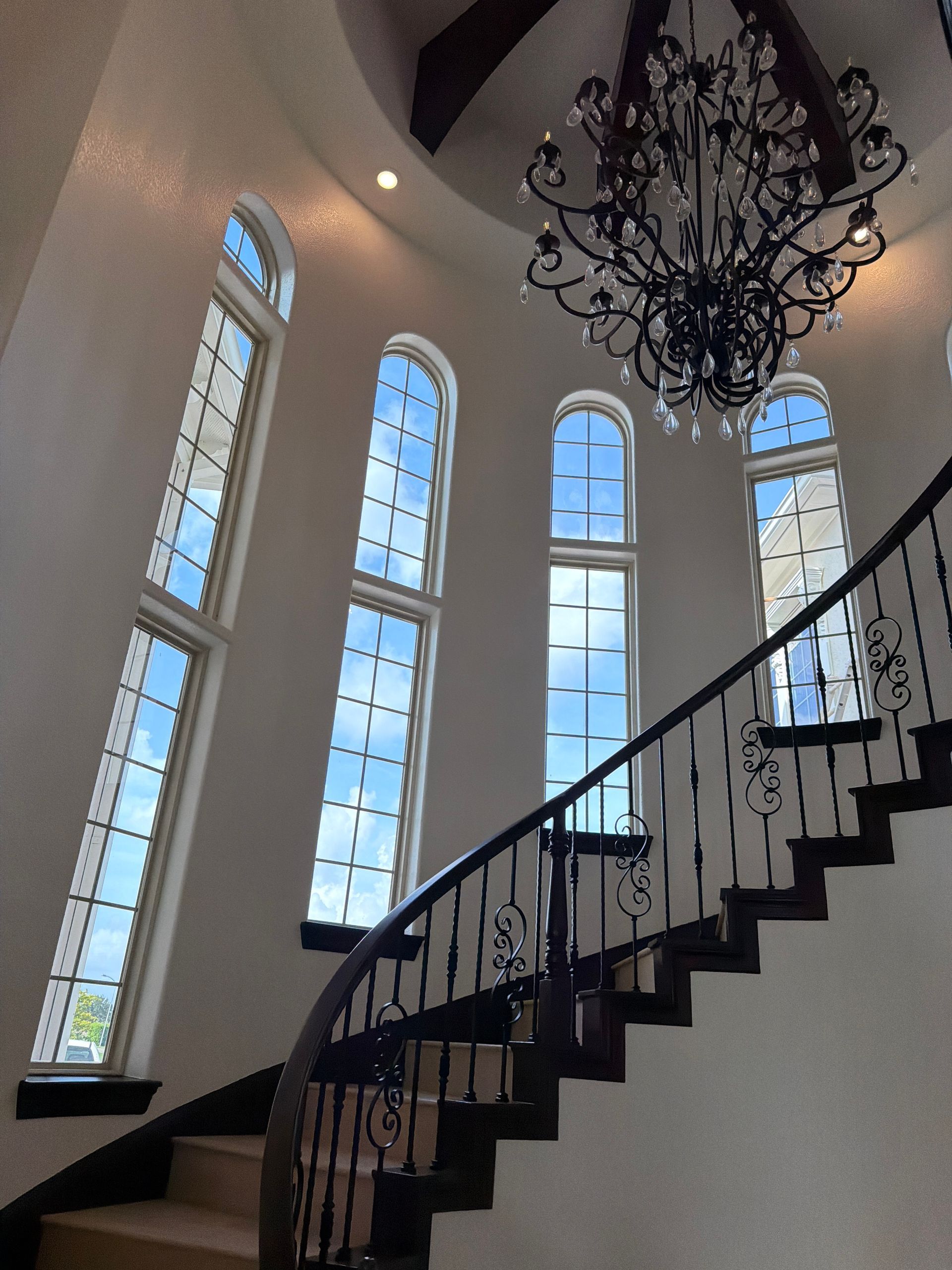 Elegant staircase with tall arched windows and a black chandelier in a bright foyer