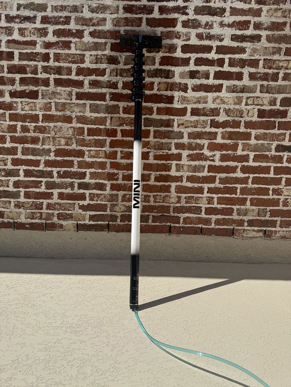Tethered pole standing on a concrete surface against a brick wall, with a blue cord attached at the base.