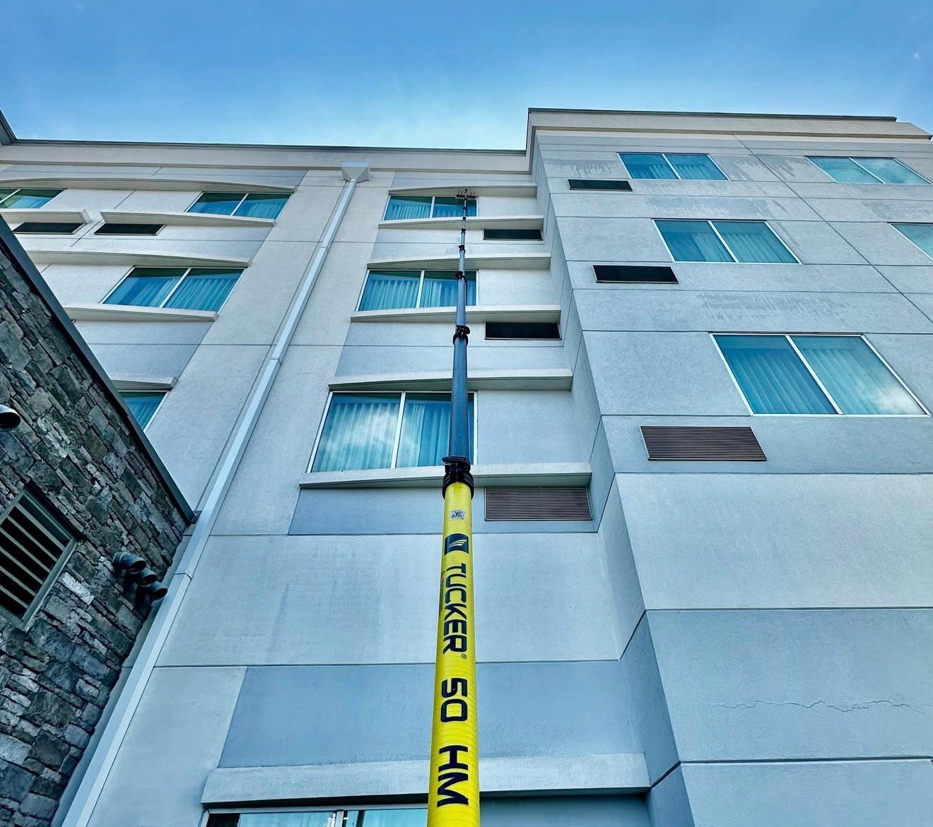 Low-angle view of a gray apartment building with blue windows and a yellow utility pole in front.