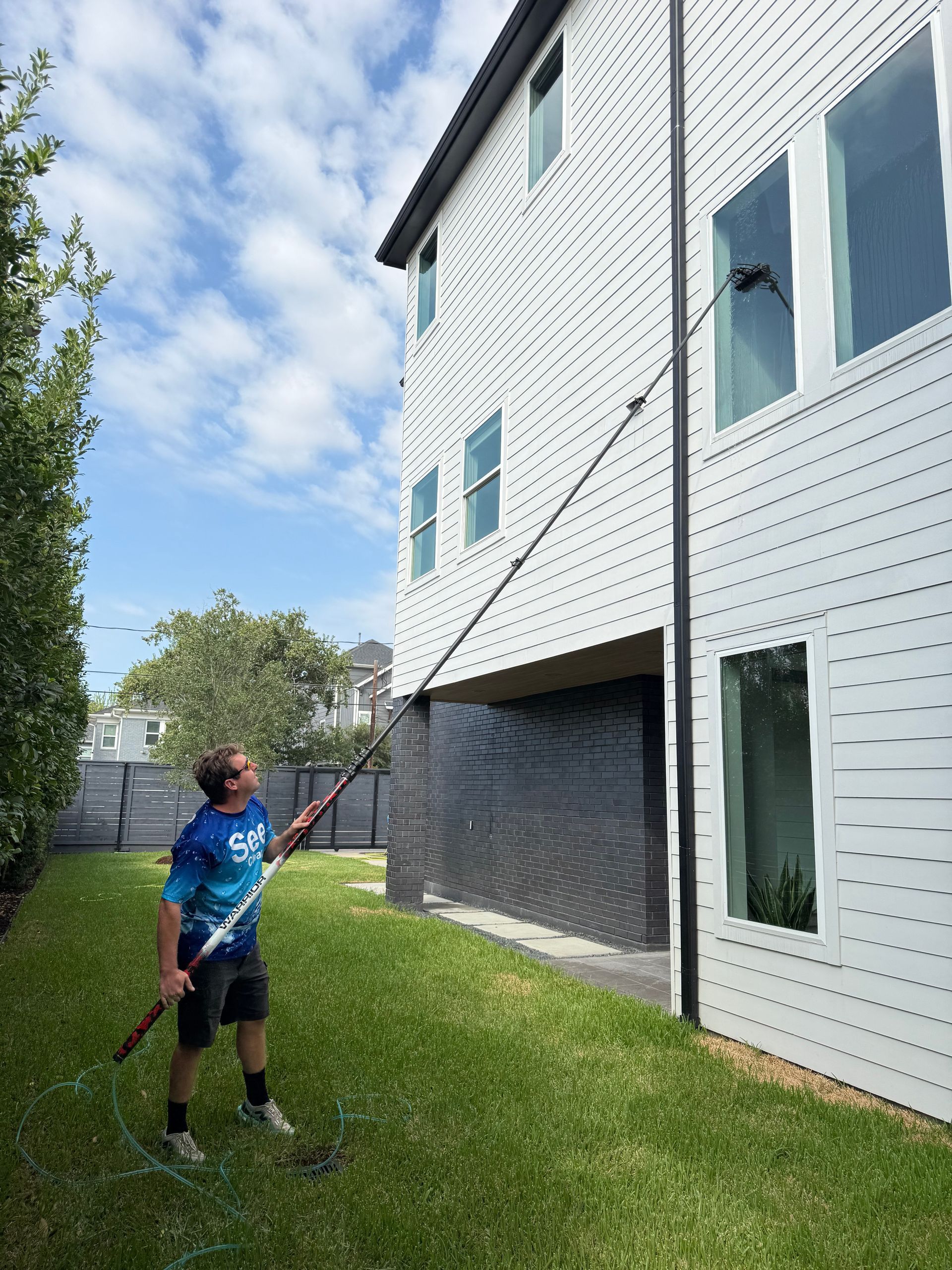 Person spraying the side of a white house with a hose in a grassy yard