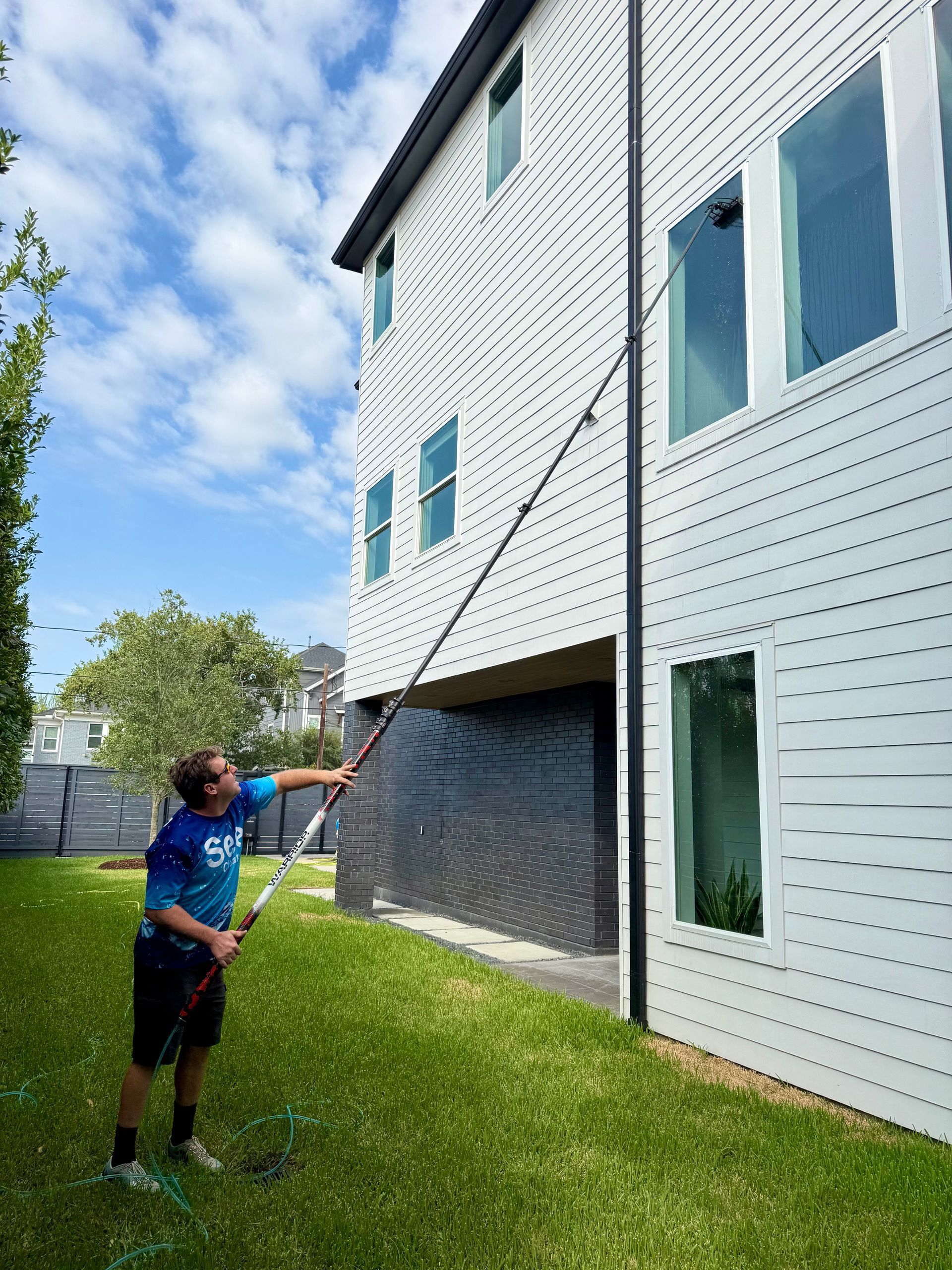 Person pressure-washing a white apartment building beside a grassy lawn.