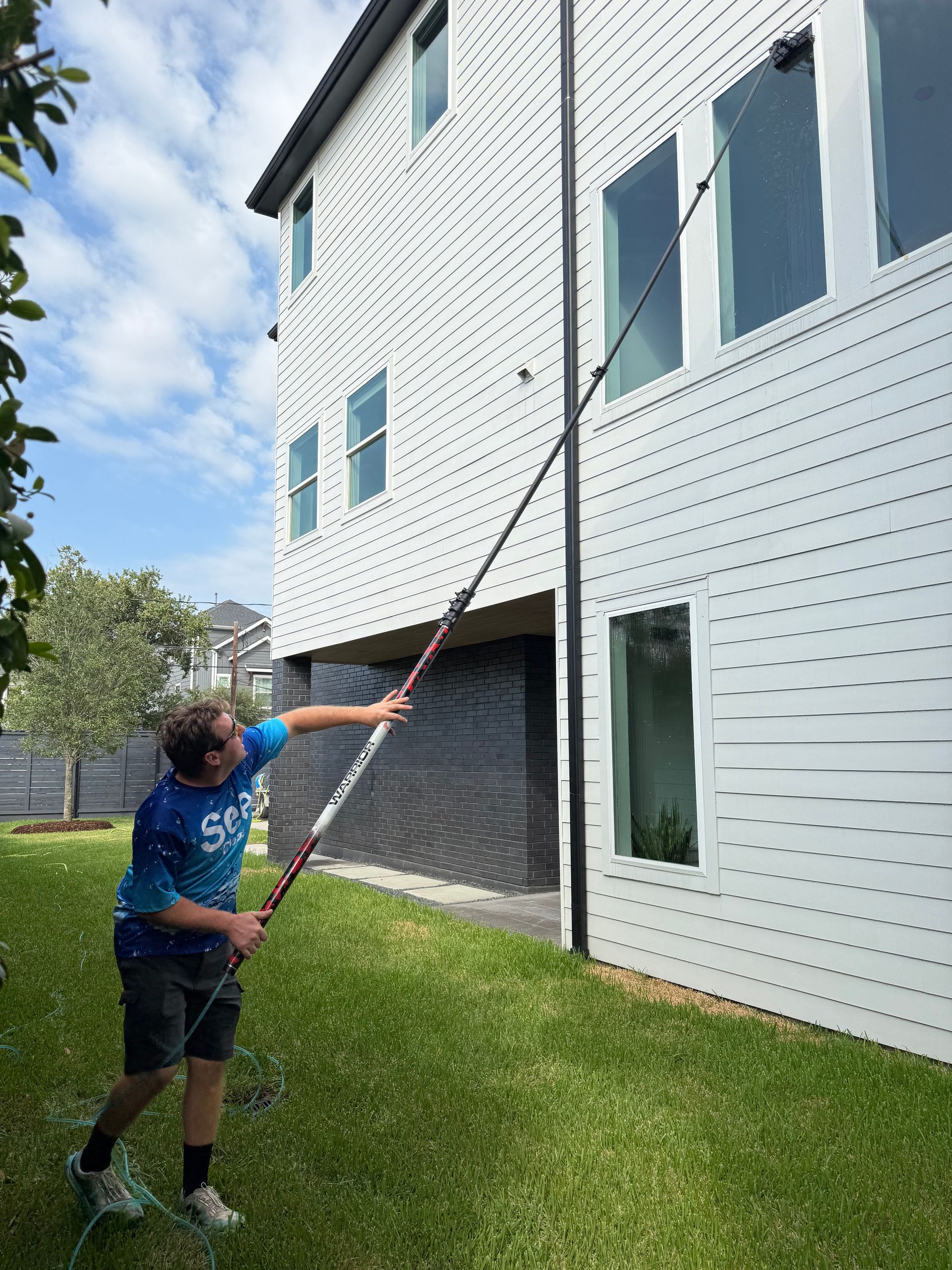 Person uses a long pole to reach the second story of a white house with dark shutters.