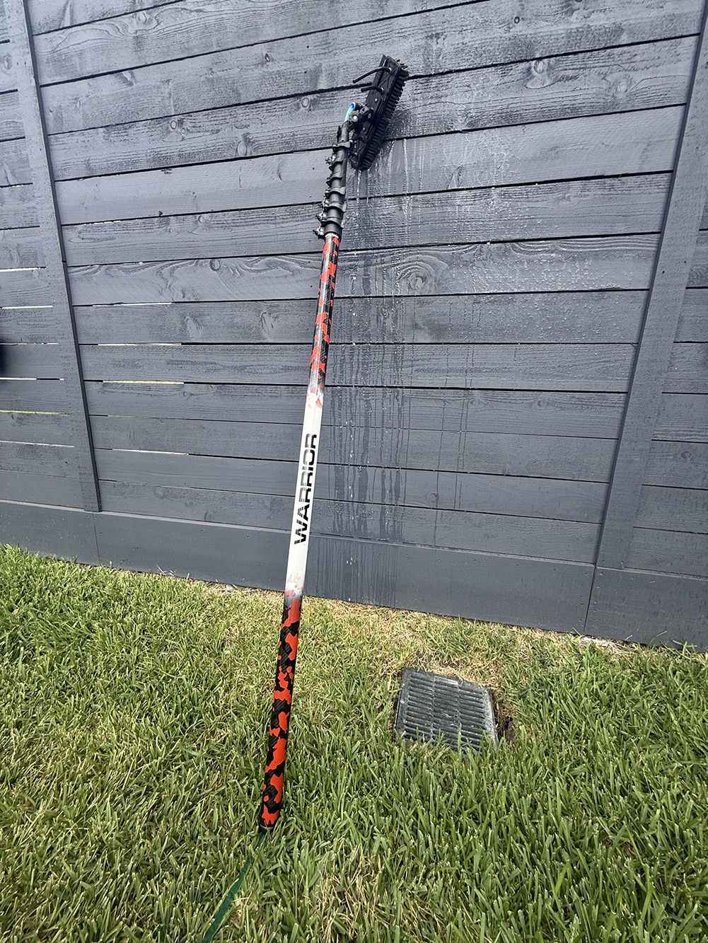 Red-and-white pole leaning against a dark fence beside a lawn with a small gray stone.