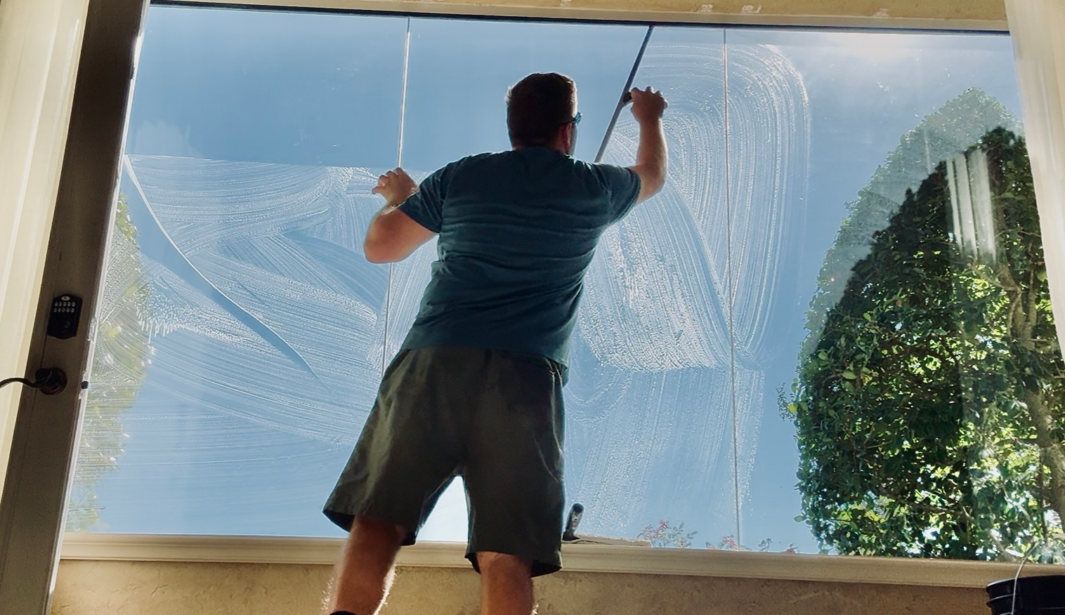 Person cleaning a large window with a squeegee, creating water streaks and reflections.
