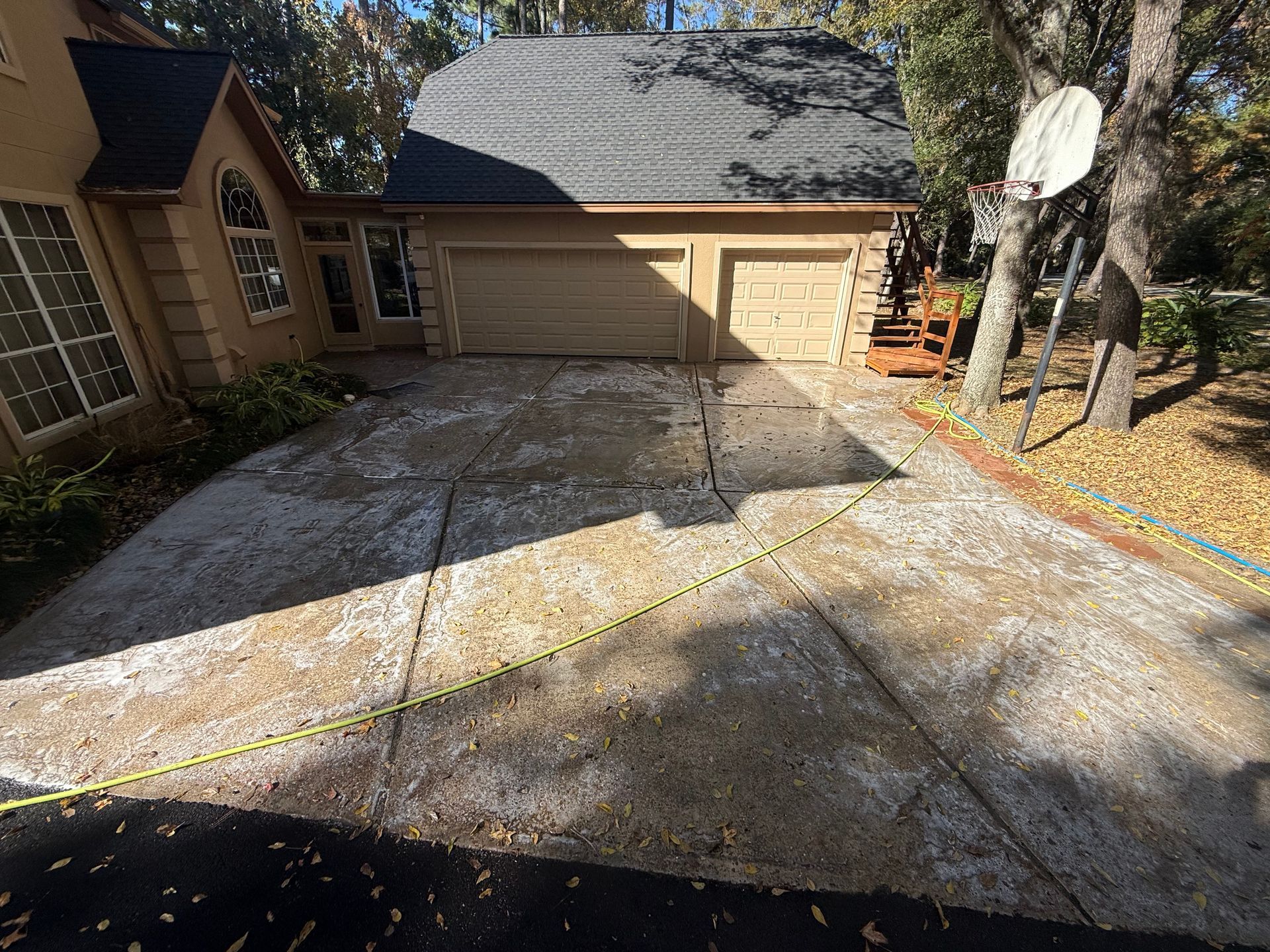 Driveway beside a house with a garage, gravel and a basketball hoop in sunlight
