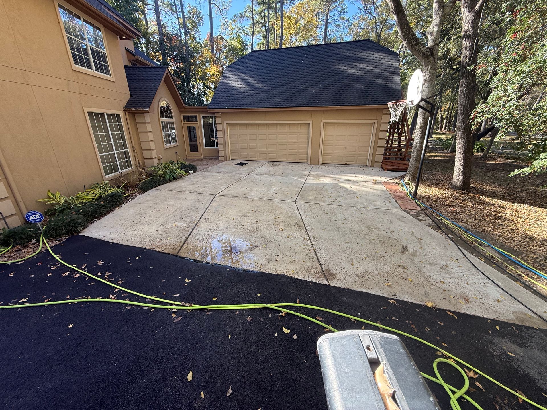 Front driveway and two-car garage beside a tan house, with black asphalt and a lime-green cord in the foreground