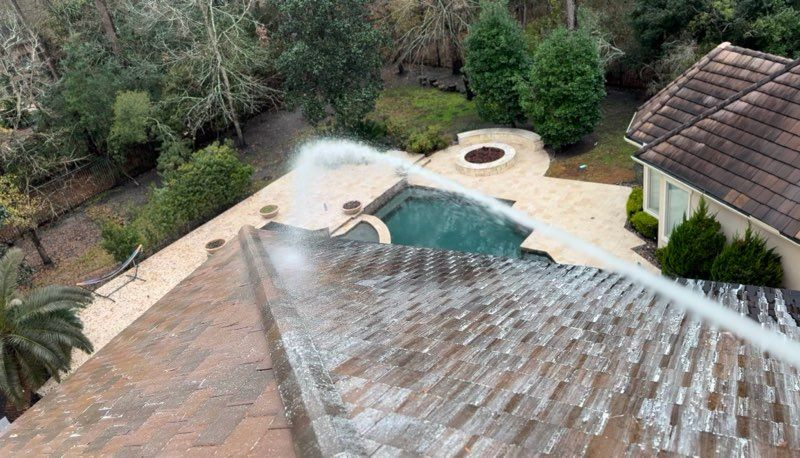 Water spraying from a roof onto a backyard pool and patio, with trees and a house nearby