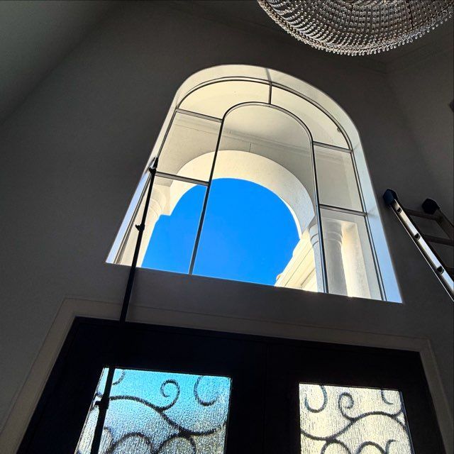 View up through a stairwell skylight with blue sky framed by arched white walls and glass doors below