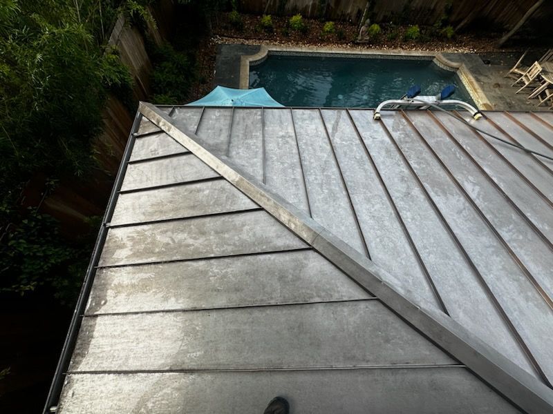 Rooftop with gray metal panels beside a backyard swimming pool and surrounding greenery