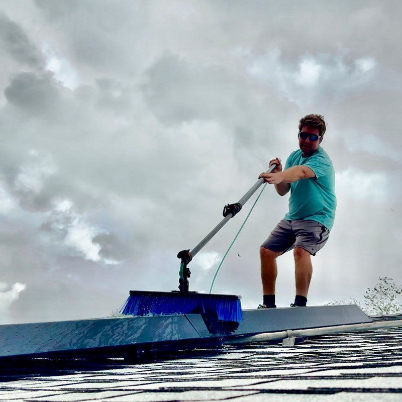 Man washing the roof with a long-handled brush under a cloudy sky