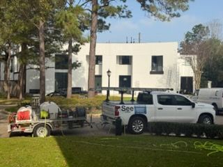 Workers and a white pickup truck with equipment in a grassy area near apartment buildings