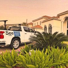White pickup truck with “See” logo parked by a villa, framed by lush greenery at sunset