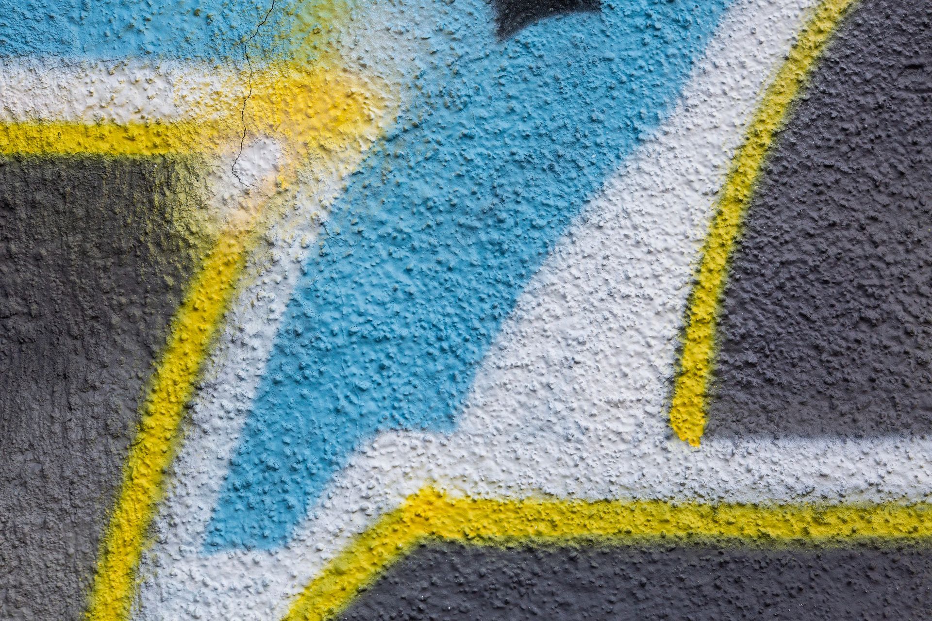 Close-up of a colorful painted mural with blue, white, yellow, and gray abstract shapes on textured concrete