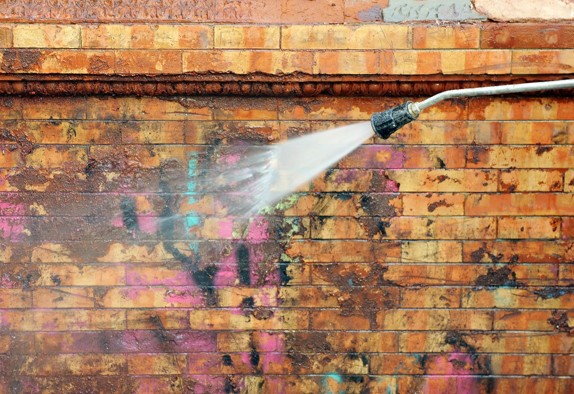 Water spraying onto a graffiti-covered brick wall, creating a misty white stream.