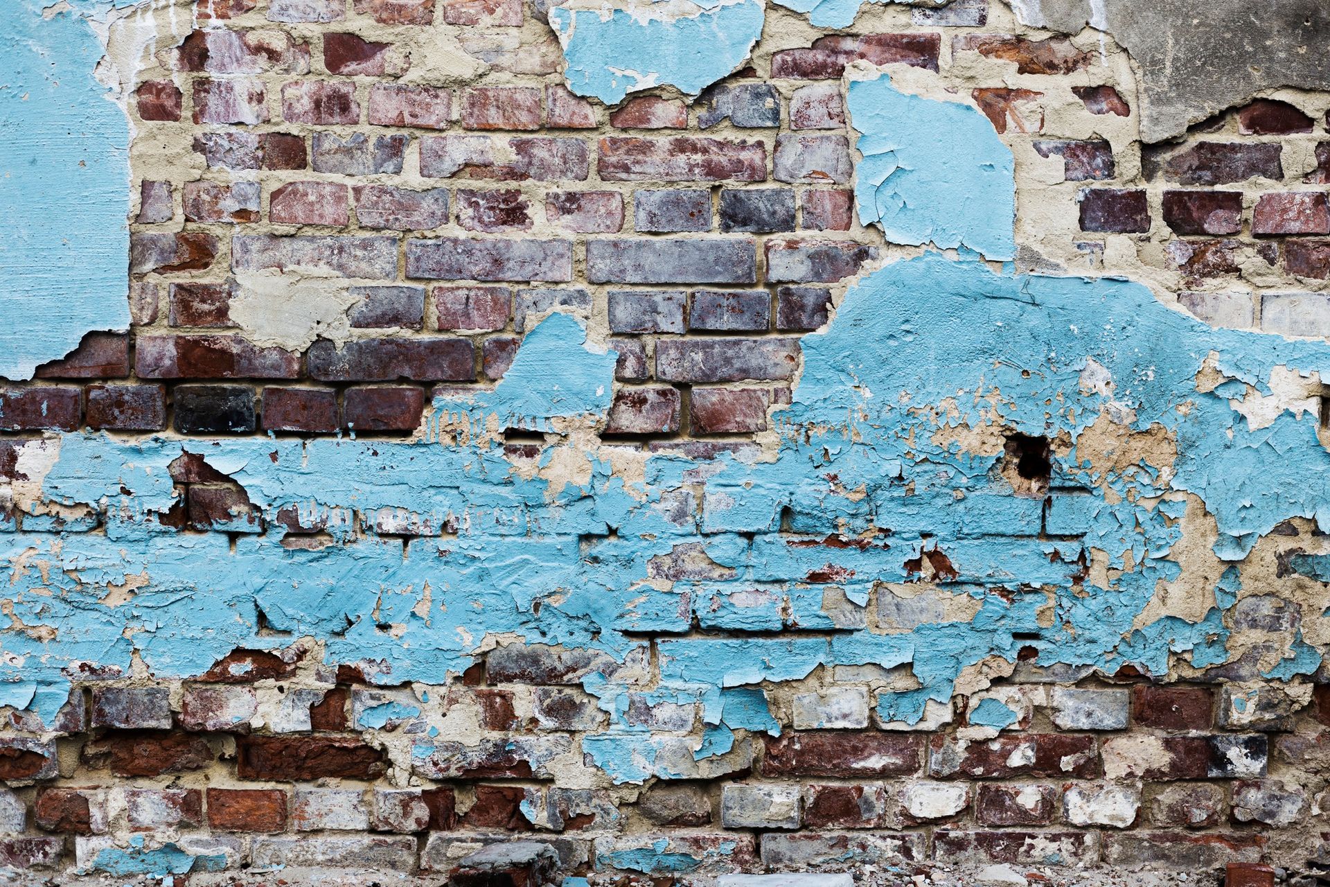Peeling blue paint on an old brick wall with exposed red bricks and weathered plaster