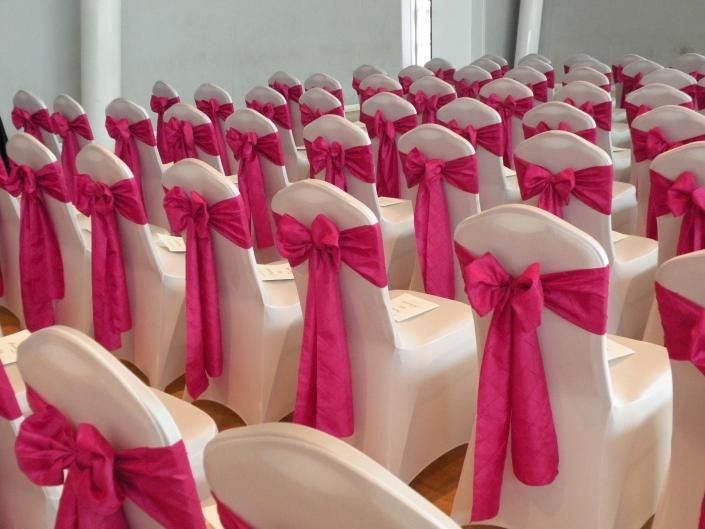 Rows of white chairs tied with bright pink bows in a decorated event hall