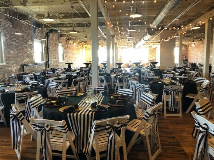 An empty industrial-style dining hall with rows of tables and chairs under warm overhead lights.