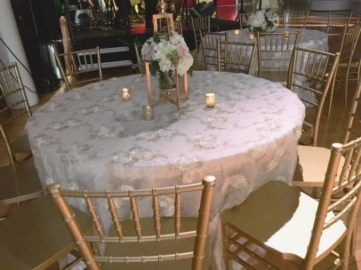 Round white floral tablecloth on a banquet table with gold chairs and candles