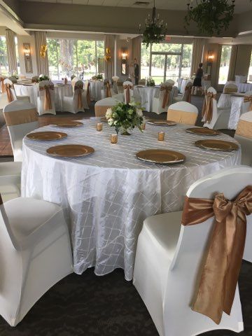 Elegant banquet hall with round tables, white chair covers, gold accents, and floral centerpieces
