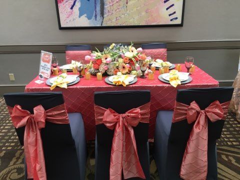 Decorated banquet table with red tablecloth, floral centerpieces, and black chairs with red bows