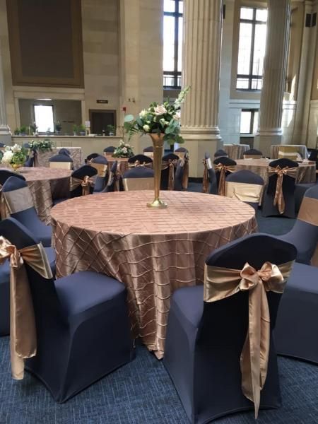 Round banquet tables with navy chair covers and gold bows in a grand hall
