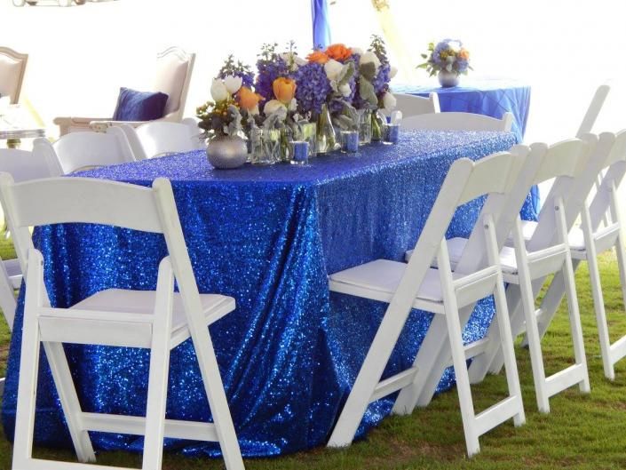 Blue tablecloth-covered banquet table with flower centerpiece and white folding chairs in a bright room