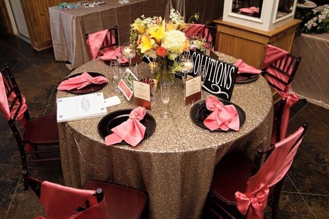 Round banquet table with gold tablecloth, pink ribbon favors, and floral centerpiece at a wedding reception