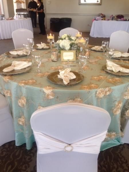 Round banquet table with aqua tablecloth, white chairs, floral centerpiece, and place settings in a reception hall