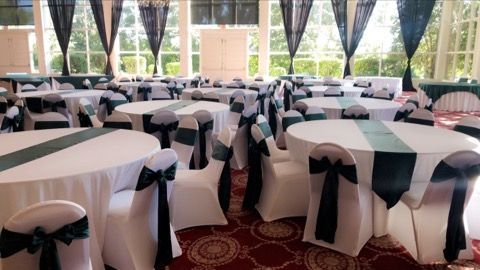 Round banquet tables with black-and-white tablecloths and white chair covers in a decorated event hall.