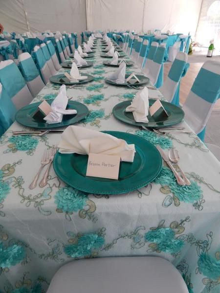 Neatly set banquet tables with turquoise accents and folded white napkins in a decorated event tent
