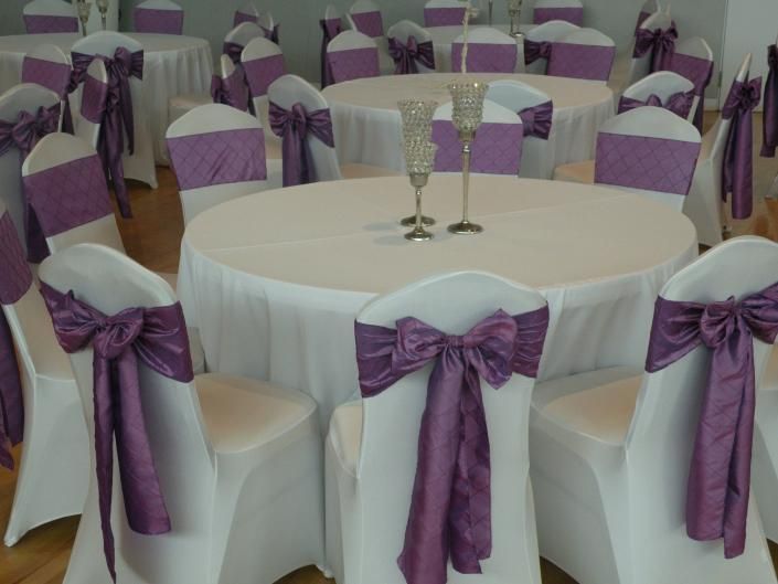 Round banquet tables with white cloths and purple chair sashes in a decorated event hall