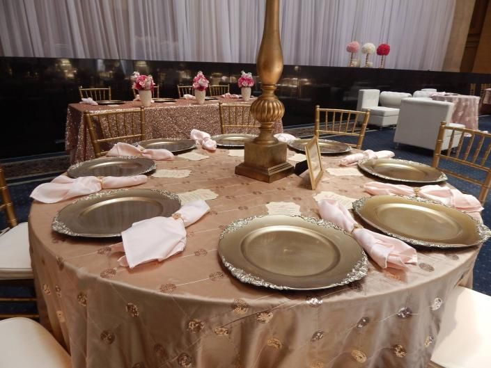 Round banquet table set with gold plates and pink napkins in a softly lit dining room