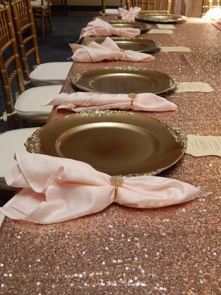 Elegant banquet table set with gold plates and folded pink napkins on a sparkling rose-gold runner.