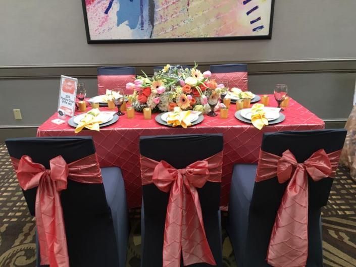 Decorated banquet table with red tablecloth, floral centerpiece, and black chairs with red bows