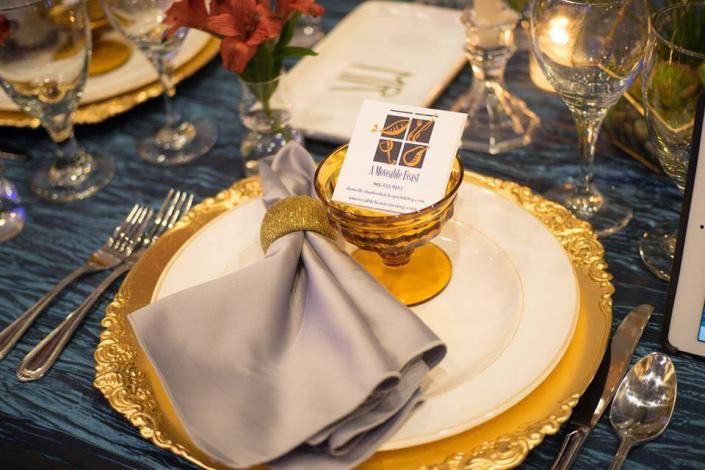 Elegant place setting with white plate, gray napkin, gold accents, and a small menu card on a blue tablecloth