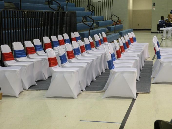 Rows of white chairs with red and blue covers in a gymnasium, set up for an event.