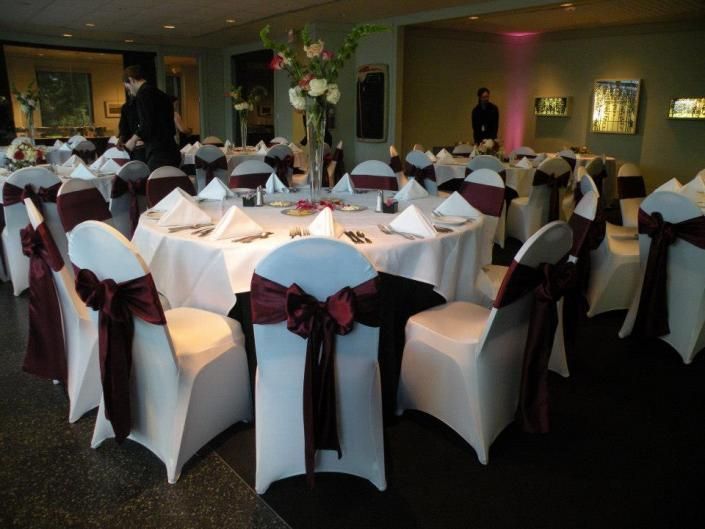 Banquet hall with round tables dressed in white and maroon chair covers, set for an event