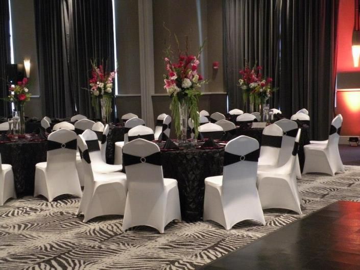 Round banquet tables with black tablecloths and white chair covers in a decorated event hall