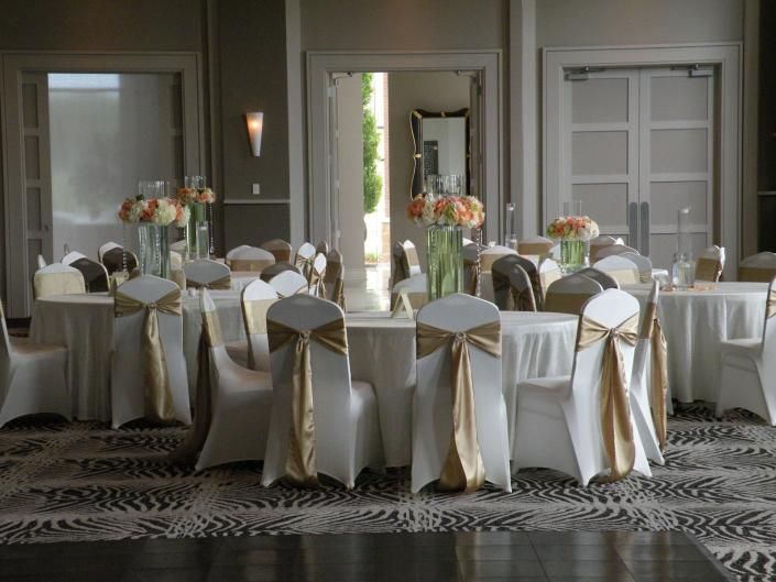 Elegant dining room set for a formal event with round tables, white chair covers, and floral centerpieces