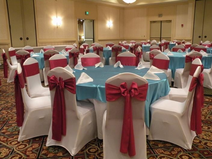 Banquet hall with round tables in turquoise and white, decorated with red chair sashes and bows