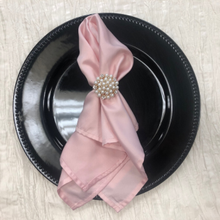 Black plate with folded pink napkin secured by a pearl napkin ring