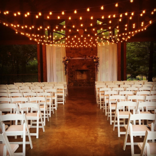 Outdoor wedding aisle with white chairs, warm string lights, and a rustic altar