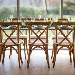 Wooden chairs around a set dining table with glassware in a bright indoor restaurant setting