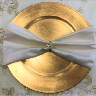 Gold charger plate with a white satin bow and jeweled center on a floral tablecloth