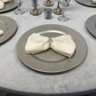Elegant table setting with a silver plate and white napkin tied with a decorative ring.