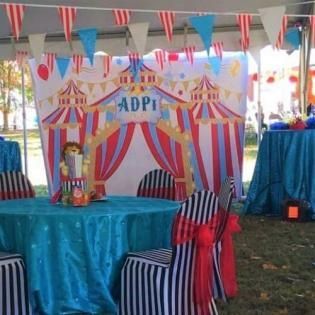 Decorated outdoor party tent with blue table, striped chairs, and a colorful backdrop labeled “ADPI”