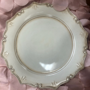 Cream scalloped decorative plate with gold trim on a pink fabric background