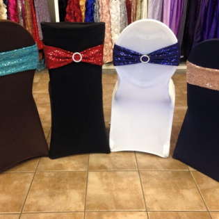 Decorated banquet chair covers in black, white, and brown with red and blue sashes on a tiled floor