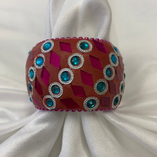 White folded fabric secured with a burgundy cuff decorated with turquoise and magenta rhinestone patterns